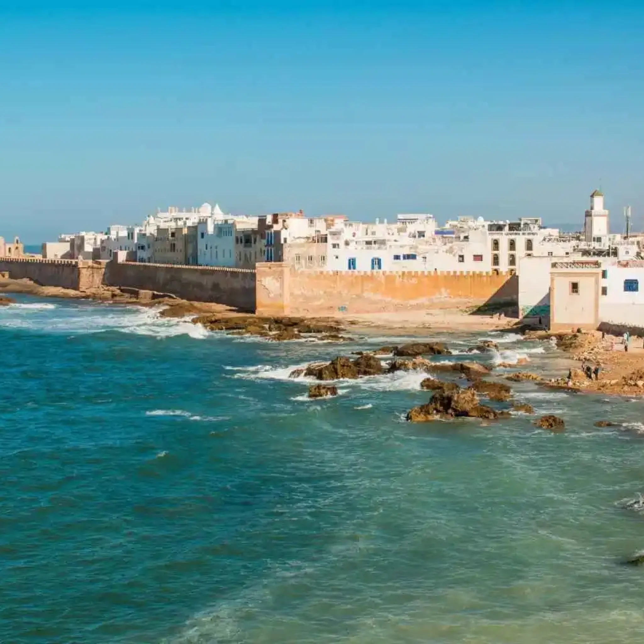 Image displaying a breathtaking moment on an Essaouira day trip, with golden sands meeting the clear blue sea under a radiant sun, encapsulating the serene beauty and charm of the location