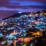 Night view of Chefchaouen, Morocco, with its iconic blue houses illuminated under a twilight sky.