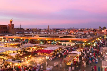 2 day trips from marrakech to merzouga : A panoramic view featuring a caravan of camels trekking towards the golden dunes of the 2 day trips from marrakech to merzouga at sunset, with the majestic Atlas Mountains in the background