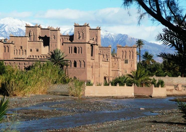 Kasbah Amridil in Skoura Oasis with flowing river and the Atlas Mountains in the backdrop.
