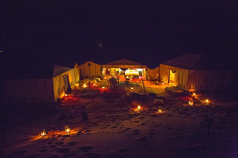 Illuminated desert camp at night with lit lanterns creating a warm ambiance in the Sahara.