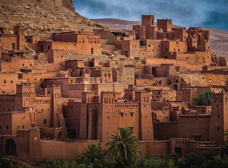 Ancient mud-brick Kasbah Ait Ben Haddou in the Moroccan desert with palm trees.