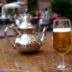 Casablanca beer bottle next to a full glass and traditional Moroccan tea set on a mosaic table.