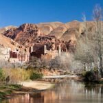 Scenic view of a river, historic Kasbah, and unique rock formations in Dades Valley, Morocco.